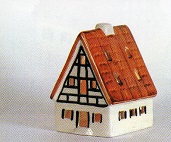 Das Bild zeigt ein Frankenhaus, gefertigt aus hochwertigem Porzellan. Es hat ein rotbraunes Dach und weie Wnden. Die Giebelfront ist mit einem Fachwerkdesign in Schwarz und Braun verziert, das an traditionelle deutsche Architektur erinnert. Das Haus ist einfach, aber detailliert gestaltet, mit kleinen Fenstern und einem kleinen Schornstein. Es wirkt handgefertigt und knnte ein Souvenir, ein Sammlerstck oder ein Dekorationsobjekt sein. Die Farben sind warm und einladend. Das Bild vermittelt ein Gefhl von Gemtlichkeit und Nostalgie, mglicherweise verbunden mit lndlichen oder traditionellen deutschen Drfern. Es ist wohl auch als Teelichthaus zu nutzen und von hinten zu beleuchten.