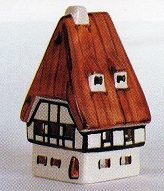 Das Bild zeigt eine handbemalte "Wache" mit einem rotbraunen Dach und weien Wnden. Das Dach ist steil und spitz, typisch fr viele traditionelle Huserarchitekturen in Europa. Das Haus ist detailliert gestaltet, mit kleinen Fenstern und einer Tr, die in einem warmen Rotbraun gehalten ist. Der Stil deutet auf ein traditionelles, vielleicht sogar lndliches Motiv hin. Das Porzellanhaus knnte ein Dekorationsobjekt sein, ein Sammlerstck oder Teil einer greren Sammlung von Husern. Die Farbgebung ist warm und einladend, und das Gesamtbild erweckt einen Gefhl von Gemtlichkeit und Nostalgie. Es knnte in einem Wohnraum, auf einem Kaminsims oder als Teil einer Dorflandschaft in einer Miniaturwelt prsentiert werden. Das Bild ist eher einfach und ohne aufdringlichen Hintergrund, wodurch der Fokus ganz auf dem handgefertigten Porzellanhaus liegt. Es ist wohl auch als Teelichthaus zu nutzen und von hinten zu beleuchten.