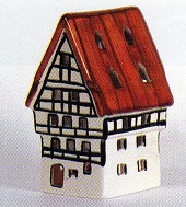 Das Bild zeigt ein detailliertes Modell einer Herberge im Fachwerkstil mit rotbraunen Dach. Das Haus ist detailreich gestaltet und zeigt typische Merkmale der Fachwerkarchitektur, wie die sichtbaren Holzbalken und die charakteristische Giebeldachform. Die Farbgestaltung ist dezent und traditionell, mit einem Kontrast zwischen dem hellen Haus und dem roten Dach. Das Modell knnte ein Souvenir oder ein Dekorationsgegenstand sein, der an traditionelle deutsche Architektur erinnert. Das Modell ist wahrscheinlich aus Pozellan oder einem hnlichen Material handwerklich gefertigt und wirkt sehr hochwertig. Es strahlt eine gewisse Gemtlichkeit und Nostalgie aus. Die przise Ausfhrung deutet auf handwerkliches Knnen hin. Das Bild selbst ist einfach gehalten und konzentriert sich ganz auf das prsentierte Hausmodell. Es ist wohl auch als Teelichthaus zu nutzen und von hinten zu beleuchten.