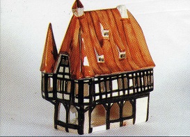 Das Bild zeigt das detailreiche Modell des Rathauses Michelstadt das im Stil eines Fachwerkhauses gestaltet ist. Das Dach ist rotbraun, die Fachwerkkonstruktion ist schwarz und wei, was auf eine traditionelle Bauweise hinweist. Das Haus hat einen Giebel und mehrere kleine Fenster, die Details zum Design hinzufgen. Die Farbgebung ist warm und einladend und ruft ein Gefhl von Gemtlichkeit und traditioneller Handwerkskunst hervor. Das Modell scheint aus Porzellan zu bestehen und ist wahrscheinlich ein Sammlerstck oder ein Dekorationsobjekt. Es reprsentiert ein Stck deutscher Architektur und Geschichte. Es ist wohl auch als Teelichthaus zu nutzen und von hinten zu beleuchten.